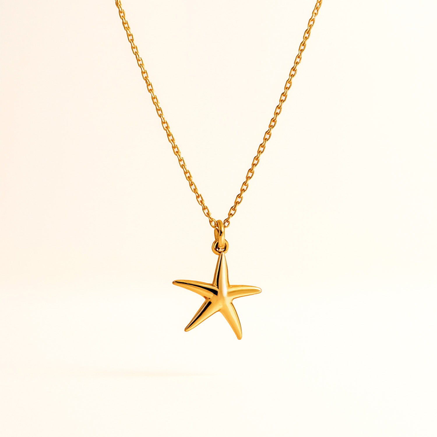 Gold starfish pendant necklace on a beige background